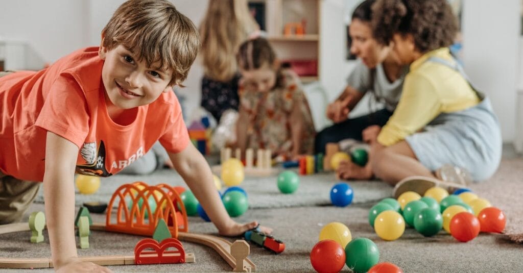 Happy children and a caregiver playing with colorful toys in a lively indoor playroom setting.
