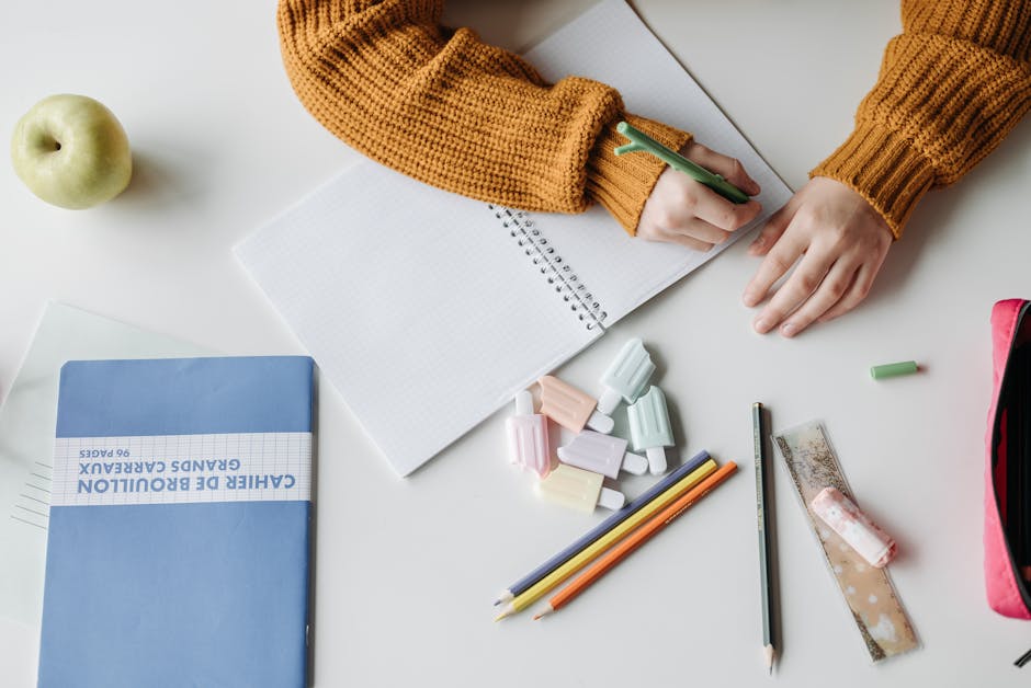 A child writing in a notebook surrounded by school supplies on a desk, featuring colorful erasers and pencils.