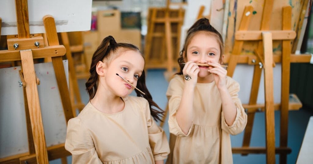 Two young girls making funny faces in an art studio surrounded by easels.