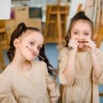 Two young girls making funny faces in an art studio surrounded by easels.