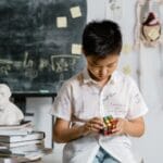 A child focuses on solving a Rubik's cube in an academic setting, reflecting intelligence and concentration.