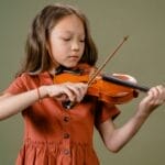 A young girl playing a violin with focus and concentration in a studio setup.