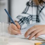 Young child learning science, writing surrounded by books and laboratory beaker.