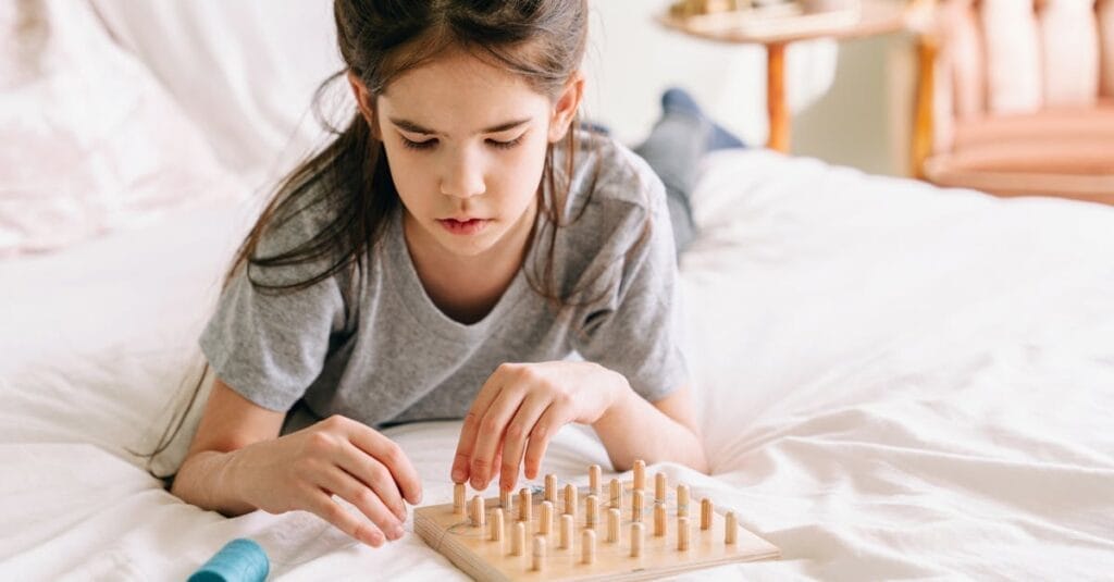 A young girl playing with a wooden geoboard on a bed, fostering creativity and learning.