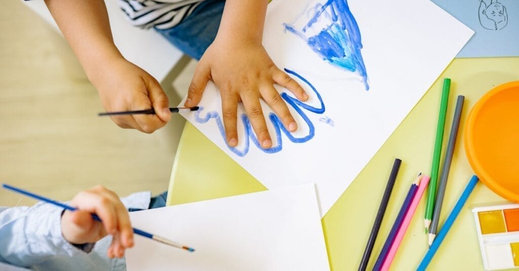 Children painting with watercolors and colored pencils, fostering creativity and learning in a fun environment.