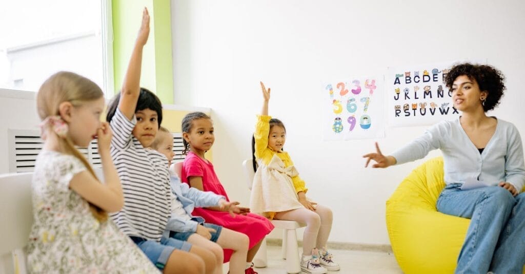 Children raising hands in classroom with a teacher, learning and engaging.