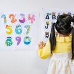 Young girl in kindergarten learning numbers and alphabets with colorful posters.