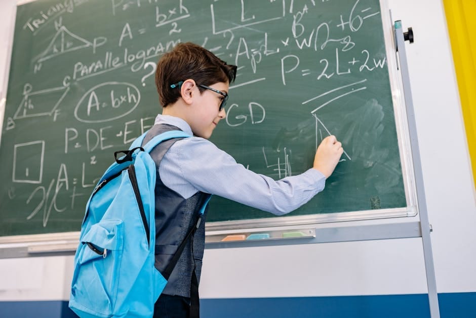 A young boy with glasses solving math equations on a classroom blackboard.