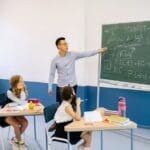 Teacher pointing at chalkboard with students in classroom learning geometry.