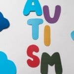 Vibrant letters spelling 'AUTISM' surrounded by blue paper clouds on a white background.