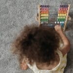 A young girl engaging with a colorful wooden abacus on a carpet, showcasing playful learning.