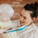 A loving mother holds her albino child while reading from a digital device at home.