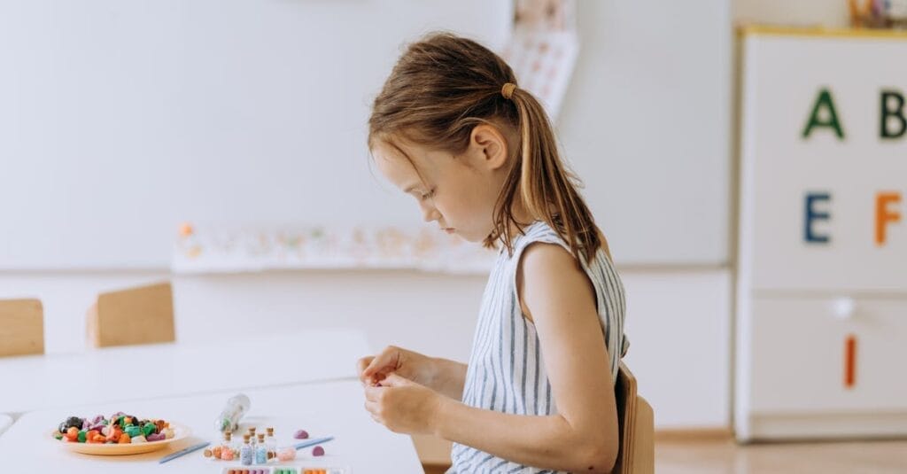 A young girl crafting with colored pencils in a bright, creative classroom setting.