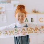 Young girl showcasing number cards in a vibrant classroom setting.