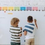 Two boys writing on a colorful classroom whiteboard, enhancing learning.