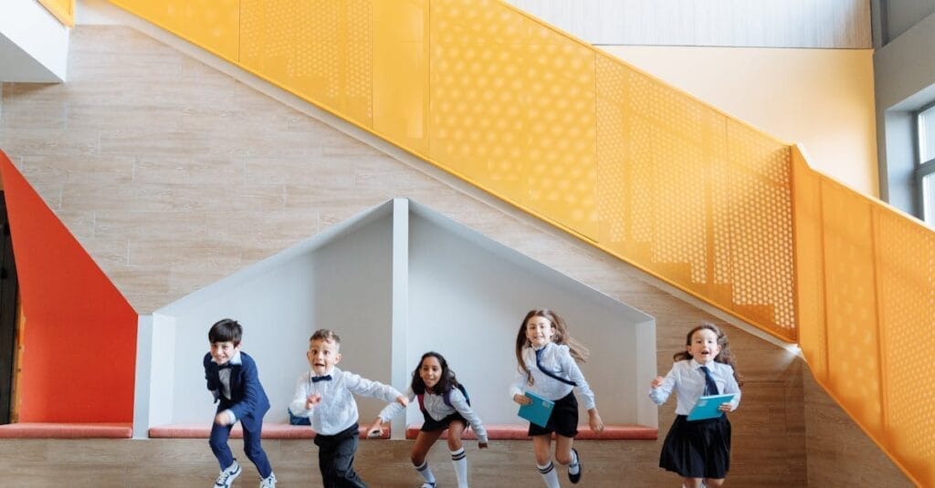 Group of cheerful children playing indoors near a colorful staircase, enjoying their school day.