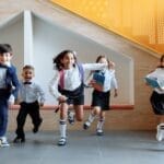 Happy school children in uniforms running energetically indoors, expressing excitement.