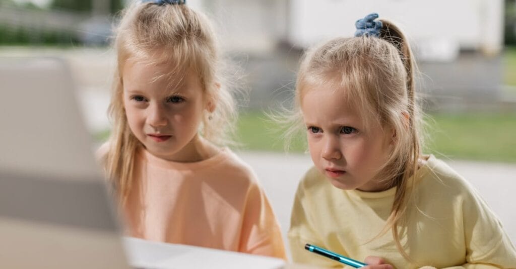 Twin girls focused on an online learning activity using a laptop.