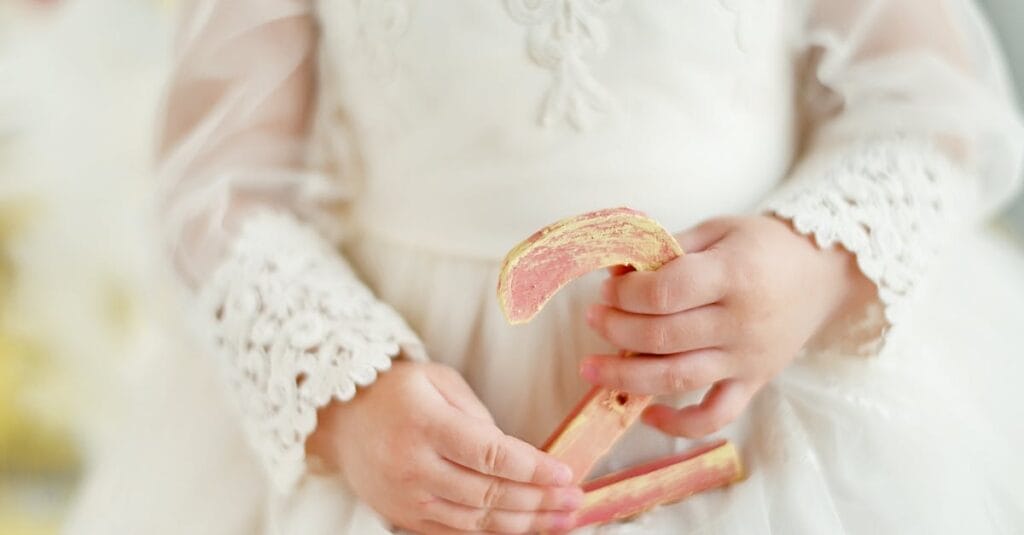 A child in a white lace dress holds a decorative number two, symbolizing birthdays or milestones.