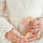 A child in a white lace dress holds a decorative number two, symbolizing birthdays or milestones.