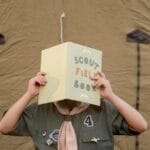 A scout child reads a field book outside a tent, embracing outdoor adventure.