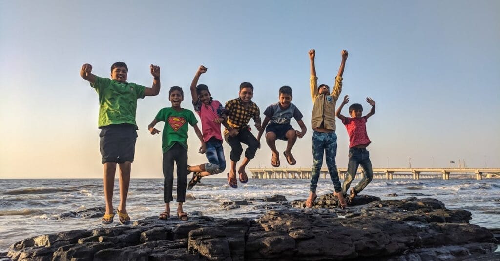 Group of kids joyfully jumping on rocks by the seaside. Fun and playful moment captured outdoors.