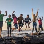 Group of kids joyfully jumping on rocks by the seaside. Fun and playful moment captured outdoors.