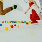 Children energetically playing with colorful balls in a bright indoor gym setting.