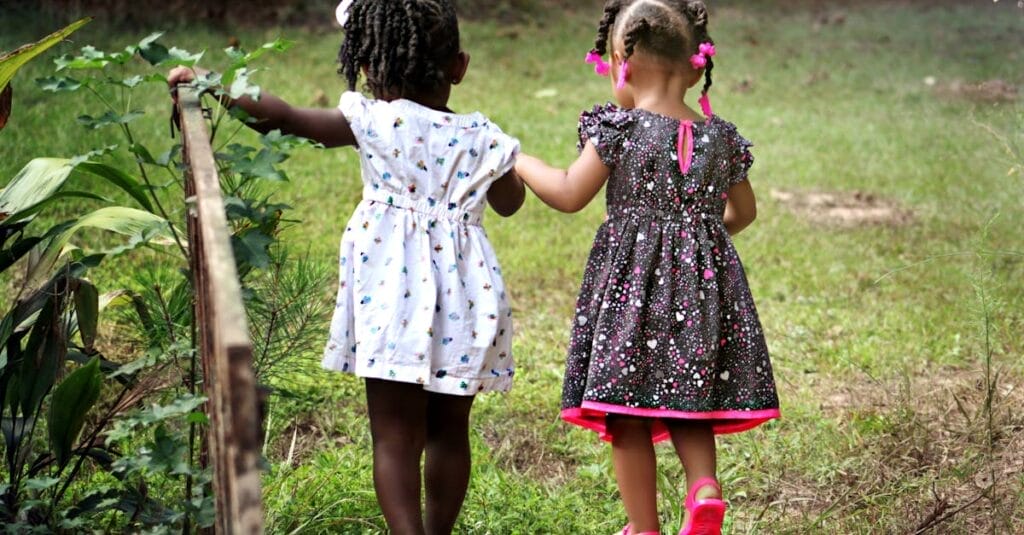 Two young girls in colorful dresses walking hand in hand outdoors, embodying friendship and innocence.