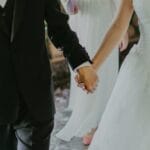 A romantic moment capturing a bride and groom holding hands in elegant wedding attire indoors.