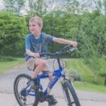 A young boy enjoys cycling outdoors in a lush green setting on a sunny day.