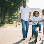 Happy family teaching their child to cycle on a sunny day outdoors.