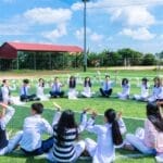 Students seated in a circle on a school field engaging in outdoor activities.