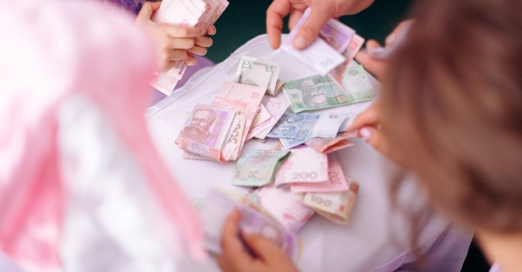 A child and adult hands sorting colorful banknotes on a table, symbolizing financial education.