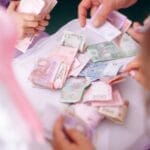 A child and adult hands sorting colorful banknotes on a table, symbolizing financial education.