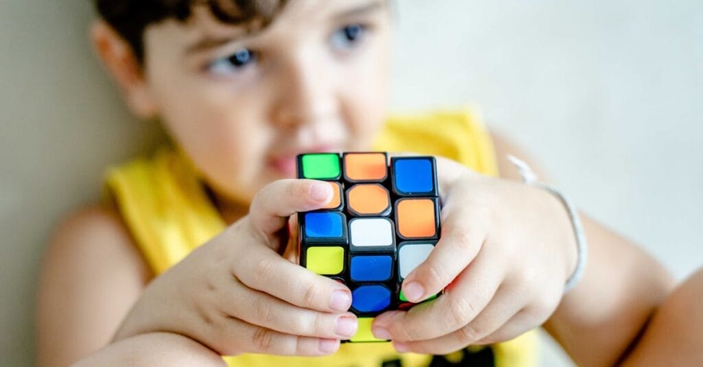 Young boy holding and concentrating on solving a colorful Rubik's Cube indoors.