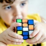 Young boy holding and concentrating on solving a colorful Rubik's Cube indoors.