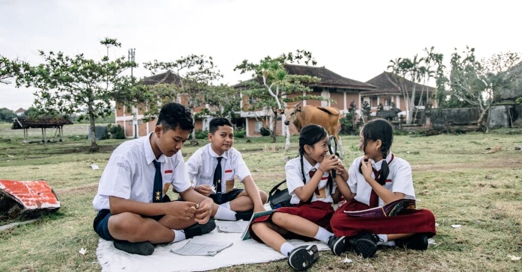 Four students in uniforms study together outside in a grassy field, embracing education and nature.