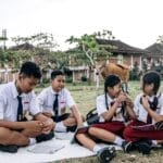 Four students in uniforms study together outside in a grassy field, embracing education and nature.