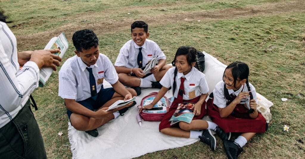 Group of students in uniforms reading together on a grassy field.