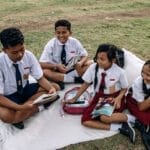 Group of students in uniforms reading together on a grassy field.