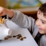 Young boy smiling while saving money in a crowned piggy bank, demonstrating financial responsibility.