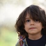 Portrait of a cute child with long hair wearing a plaid shirt, standing outdoors during spring.