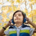 A young boy enjoys music through headphones amidst colorful fall foliage.