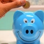 Hand inserting a coin into a blue piggy bank for savings and money management.