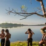 Five kids enjoy a playful day by the lake, climbing trees and bonding under clear skies.