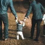 A family of four walks hand in hand on a path, enjoying a sunny day outdoors.