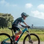 A young boy in sportswear rides a mountain bike on a rural dirt road during a sunny summer day.