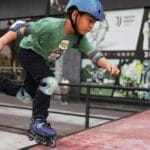 A boy performing a move on roller skates at a skatepark, wearing protective gear.