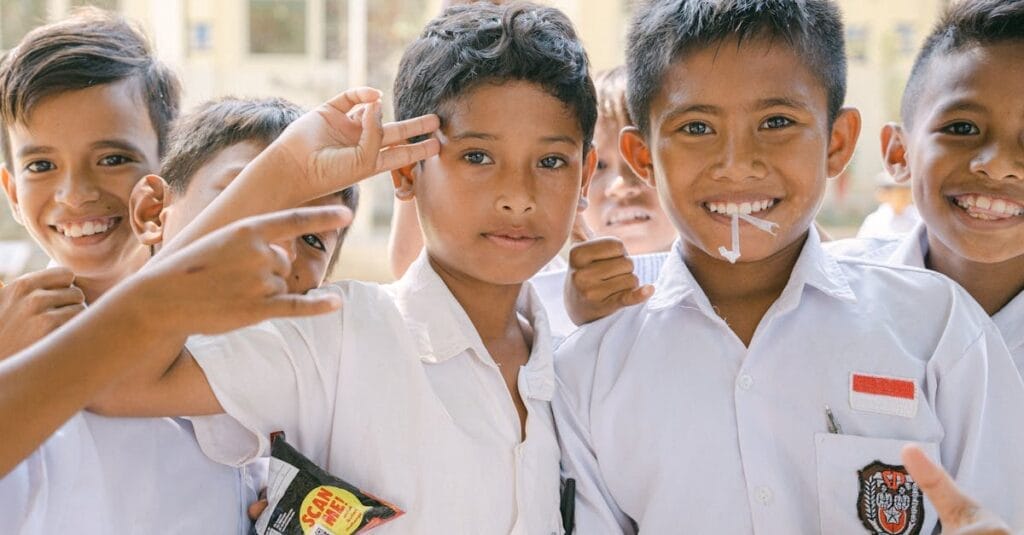 Joyful Indonesian schoolboys in white uniforms smiling and posing outdoors.